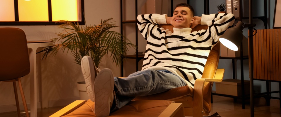 Young man relaxing in a leather chair at home with his feet up, enjoying a safe and comfortable spring break indoors — a reminder that spring break safety includes knowing when to unwind responsibly.