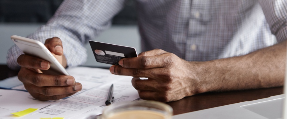 Close-up of a person holding a credit card and smartphone over financial documents, visually illustrating how insurance rates are determined by reviewing credit history.