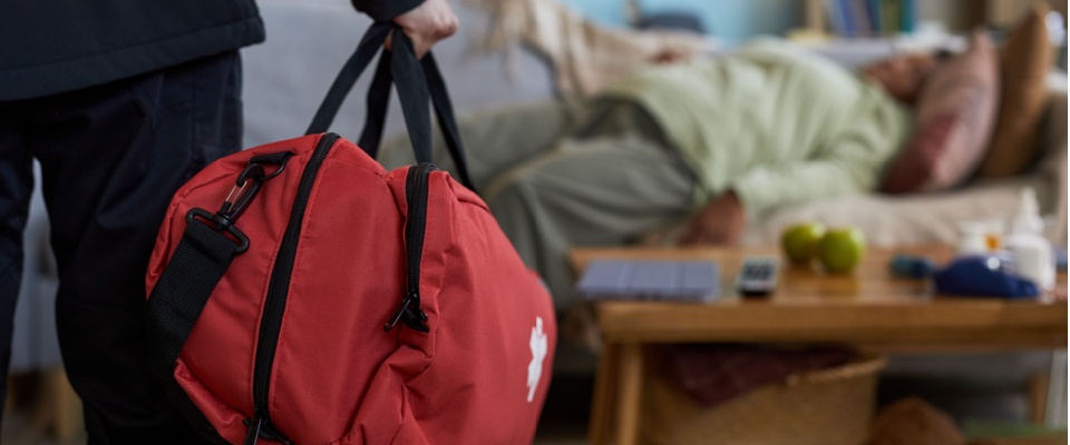 First responder carrying a medical bag while assisting a person on a couch, highlighting the importance of having an updated emergency contact list during a health crisis.