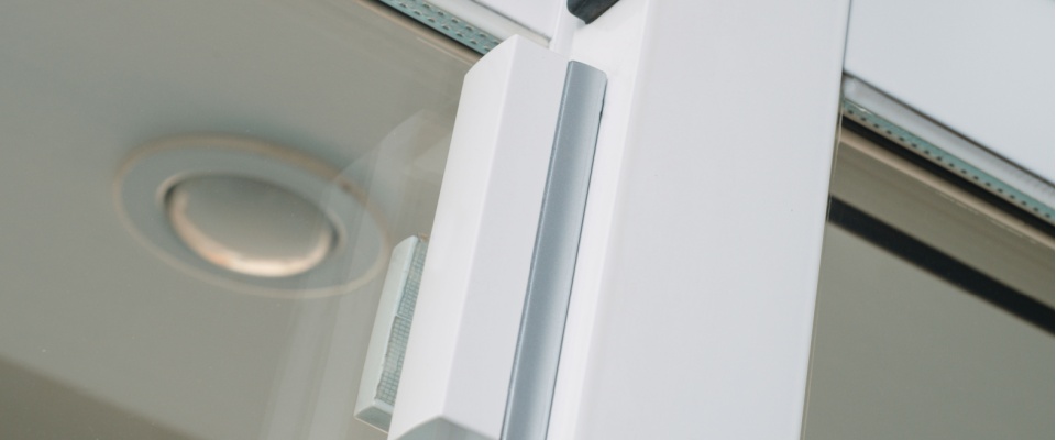 Close-up view of a modern window sensor installed on a glass door, used to deter burglars.