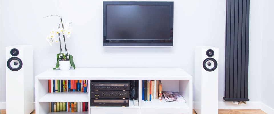 A modern living room entertainment setup with a flat-screen TV, speakers, books, electronics, and decor neatly arranged on white furniture, visually illustrating the importance of assessing your personal belongings to determine how much renters insurance you need.