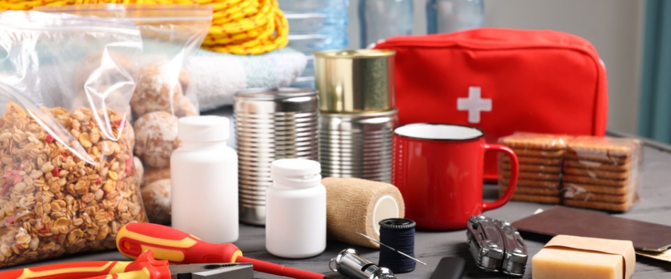 A collection of emergency preparedness items — non-perishable food, bottled water, medical supplies, tools, flashlight, and first aid kit, in additional to renters insurance coverage for hurricane damage.