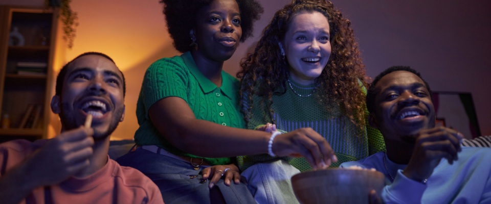 A group of friends relax together on a sofa in a cozy, softly lit living room, sharing snacks and enjoying each other's company, visually illustrating the importance of lifestyle questions to ask potential roommates.