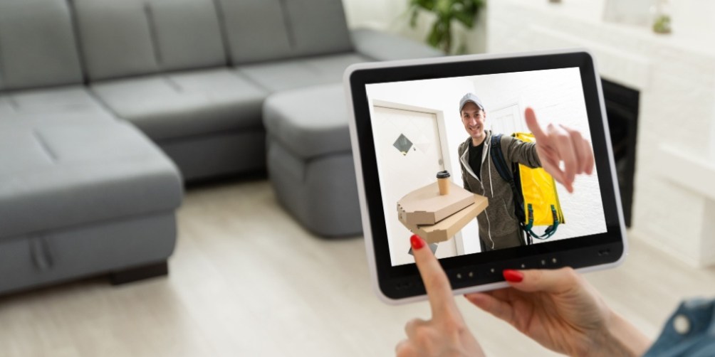A person using a smart home tablet in a cozy living room to view a delivery person at the front door, illustrating how renter-friendly security systems provide extra peace of mind and convenience.