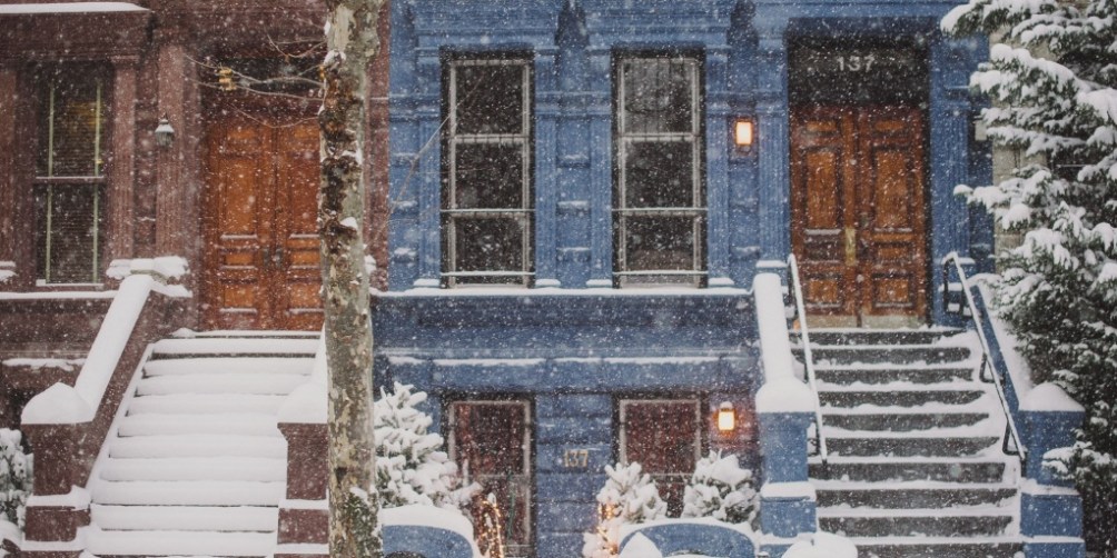 Snow-covered row houses and icy steps during a storm, reinforcing the importance of snow shoveling safety for walkways and entrances.