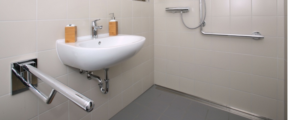 A modern, accessible bathroom features sturdy grab bars, a wall-mounted sink, and an open shower area designed for safety and easy mobility for seniors when downsizing.