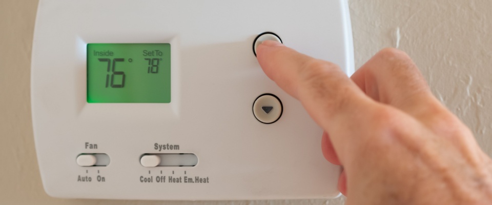 Close-up of a hand adjusting a digital thermostat to a higher temperature, demonstrating how to lower the electric bill in summer by setting the thermostat efficiently while at home.