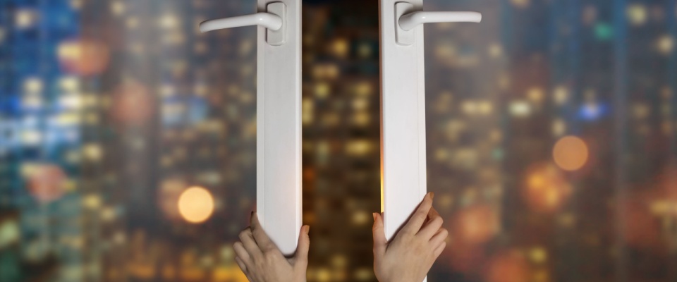 Hands opening a window at night with city lights in the background, using natural ventilation to cool the apartment and lower the electric bill in summer.