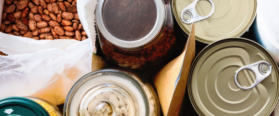 Assorted jars and cans of beans, grains, and dry foods arranged closely together, showing a practical selection of non-perishable food supplies to include in a power outage emergency kit.