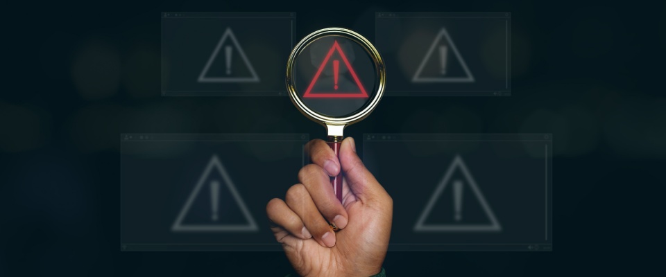 Hand holding a magnifying glass over a red warning symbol, highlighting the importance of vigilance and reporting rental scams.