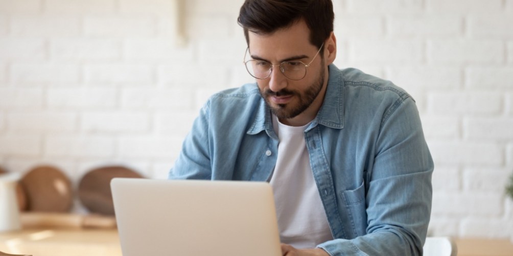 Man in casual clothes sitting at a desk using a laptop in a bright home office, looking into how to cancel renters insurance.
