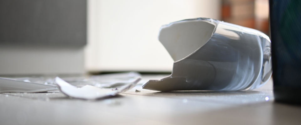 Close-up of a broken glass cup shattered on a tiled floor, illustrating a lesser-known renters insurance benefit that can cover accidental damage to someone else's property.