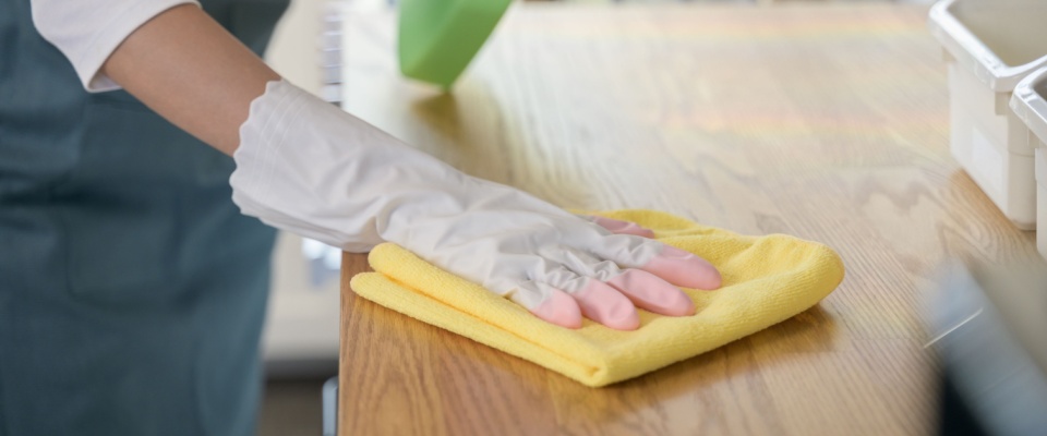 Person wearing cleaning gloves wiping down a wooden countertop, a key kitchen task included in a holiday cleaning checklist.