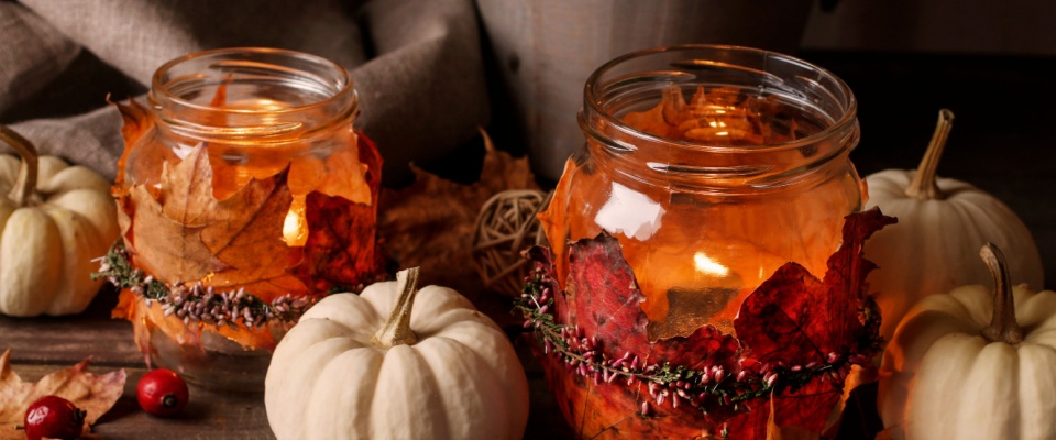 DIY glass jar candle holders decorated with autumn leaves and surrounded by small white pumpkins and berries, providing some creative fall decor ideas.