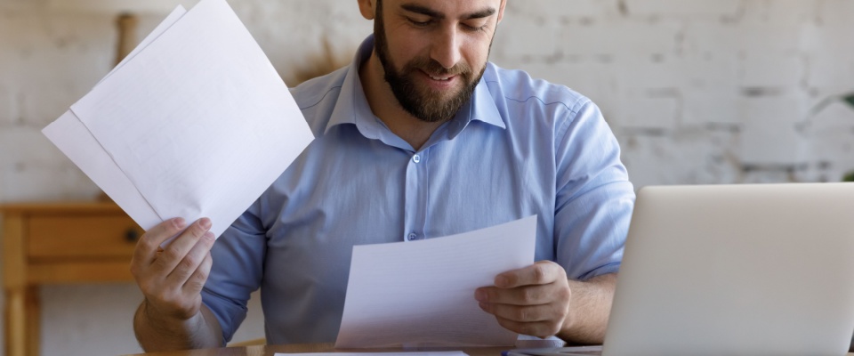 Man in a blue shirt sitting at a desk with paperwork and a laptop, illustrating renters insurance mistakes such as skimming policy details.