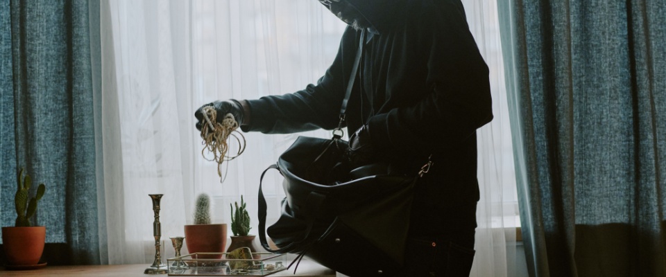 Burglar placing stolen jewelry into a bag, illustrating why renters and homeowners need high-value item coverage for theft protection.