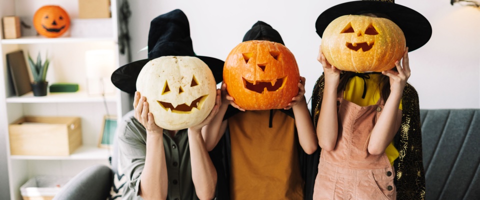 Kids wearing witch hats and holding carved pumpkins in front of their faces, celebrating the holiday while promoting Halloween safety.