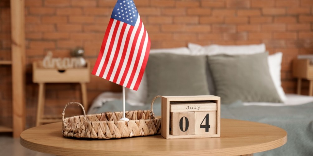 Wooden table with a small American flag and a calendar block displaying July 4th in a cozy bedroom, serving as a reminder for 4th of July safety tips in an apartment.