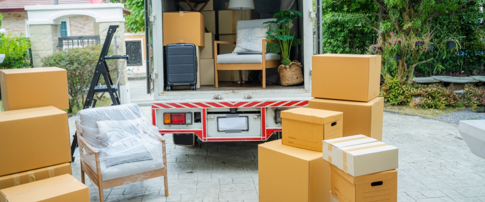 Moving truck parked in driveway with cardboard boxes, furniture, and household items being loaded or unloaded, illustrating the benefits of renters insurance coverage during moving.