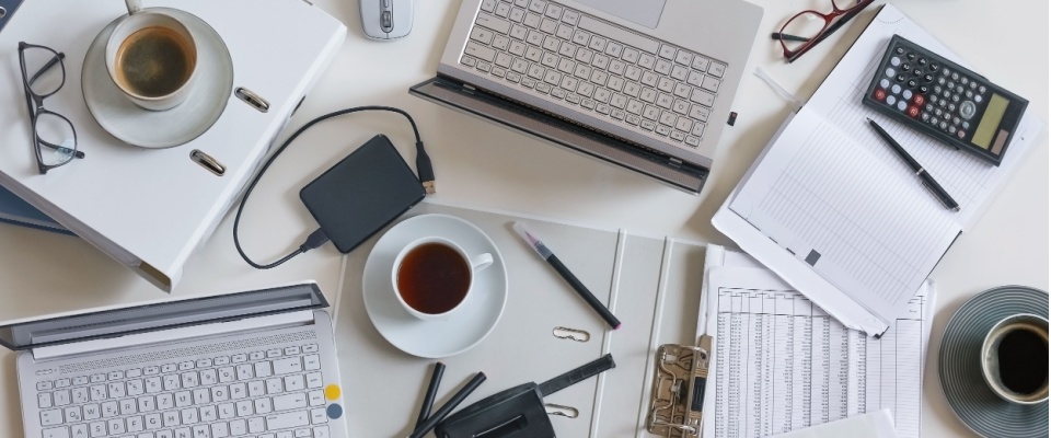 Overhead view of a busy home office desk with laptops, coffee cups, files, stationary, calculator, and documents, showcasing what can be covered by renters insurance when working from home.