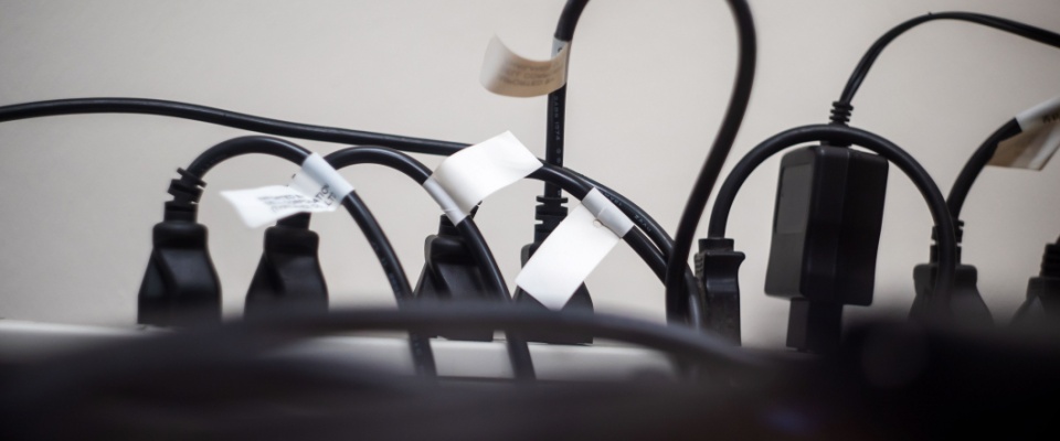 Multiple power cords and plugs connected to an outlet strip with labeled tags, illustrating work-from-home safety by practicing proper electrical organization and reducing fire hazards in a home office setup.