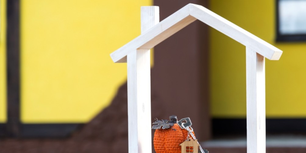 Miniature house frame with keys and a pumpkin decoration symbolizing home protection and renters insurance coverage during Halloween.