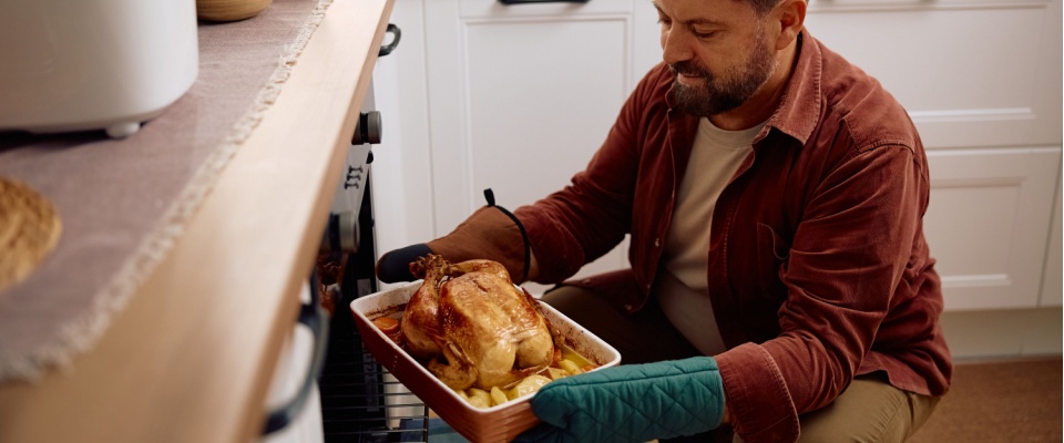 Man placing a roasted turkey into the oven, highlighting Thanksgiving safety tips for cooking and avoiding kitchen fires.