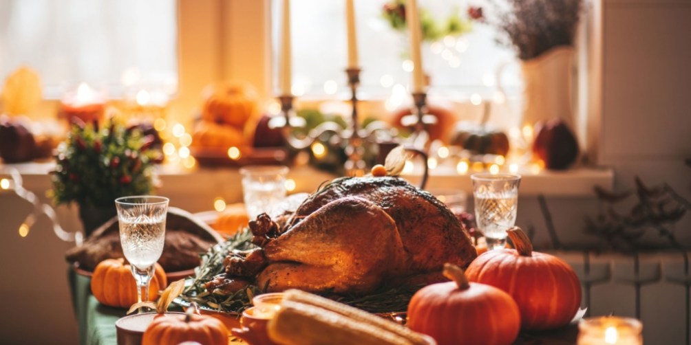 Thanksgiving dinner table with turkey, pumpkins, and candles, reminding readers of Thanksgiving safety tips for a worry-free holiday.