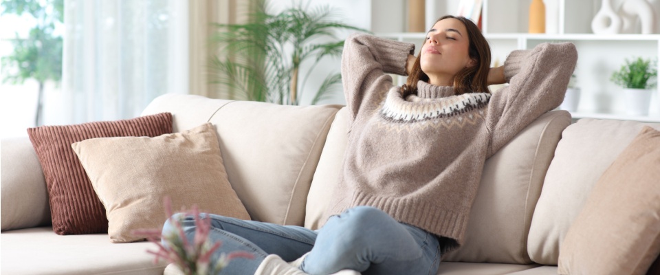 Woman relaxing on a couch at home after traveling, highlighting winter vacation safety tips for returning to a comfortable and secure home.