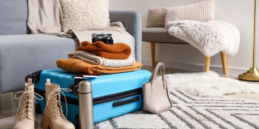 Packed suitcase with winter clothing and travel essentials in a living room, emphasizing winter vacation safety preparation before leaving home.