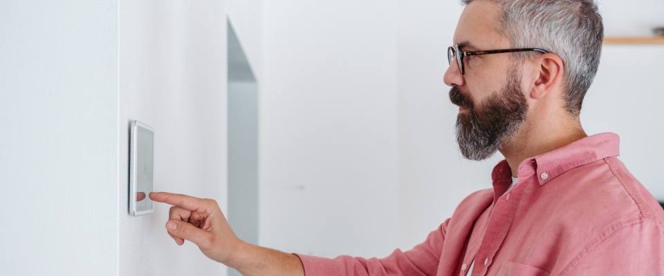 Man adjusting a smart thermostat on the wall, an important step to winterize your apartment and maintain energy-efficient heating.