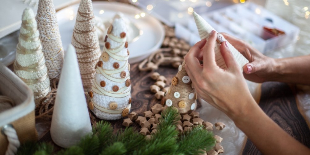 Hands crafting small decorative Christmas trees with buttons and yarn as part of a cozy DIY holiday decoration project.