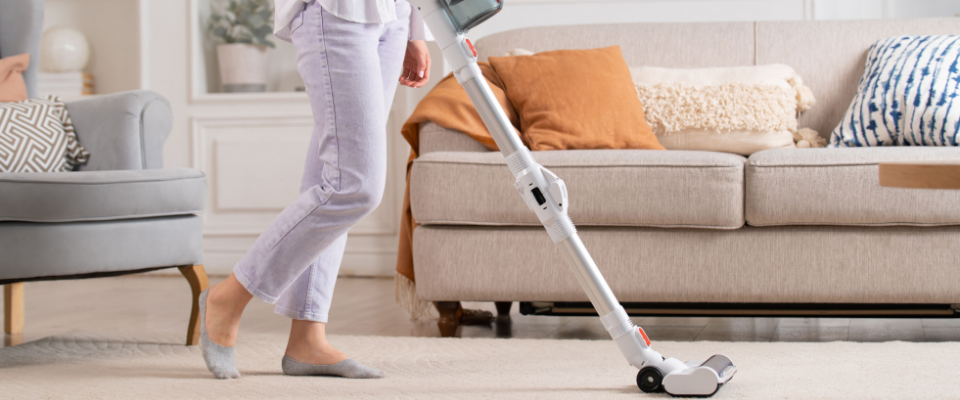 A person using a cordless vacuum to clean a light-colored rug in a bright living room, as part of their spring cleaning checklist.