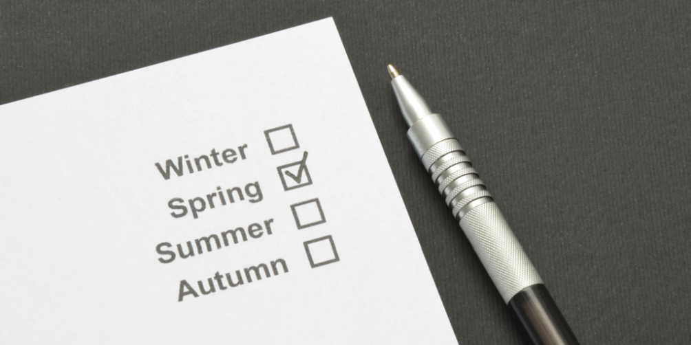 Cleaning checklist for seasonal organization with a marked checkbox for 'Spring' on white paper next to a silver pen.
