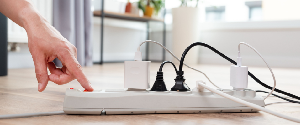 A person turning on a white power strip with several plugs connected, highlighting the importance of electrical safety at home.