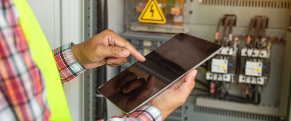 Electrician using a tablet to inspect an electrical panel, planning to set up electricity in an apartment.