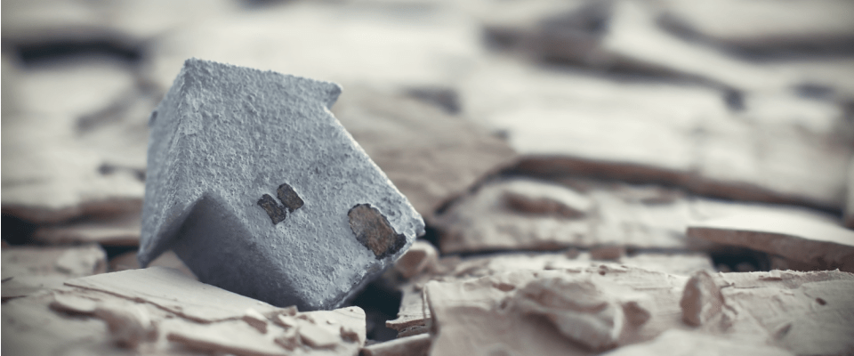 Close-up of a small house model on dry ground, highlighting what renters insurance doesn't cover, such as natural disasters and structural damage.