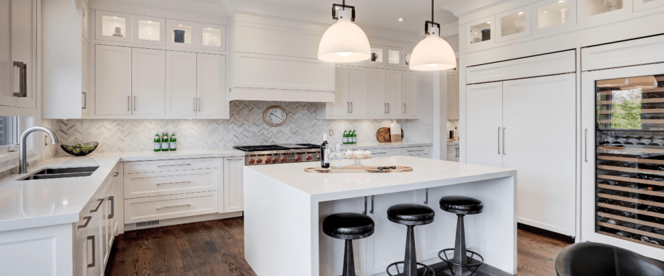 Clean and stylish white kitchen featuring a countertop island, hanging lights, storage cabinets, and appliances in good condition, where following electrical safety tips helps prevent accidents.