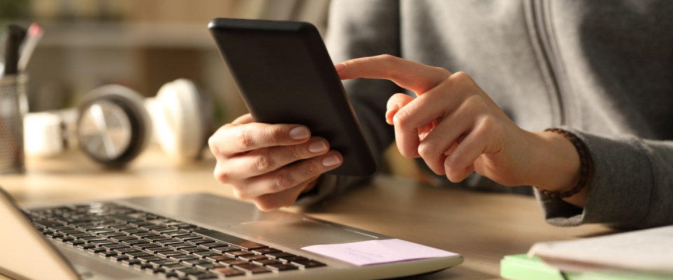 Close-up of a person using a smartphone in front of a laptop and paperwork on a desk, calling utility companies and considering all-bills-paid apartments.