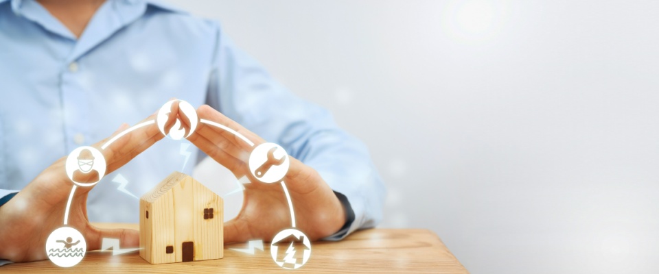 Person shielding a small wooden house model with hands, surrounded by icons of fire, theft, flooding, and electrical damage, illustrating why you need renters insurance for comprehensive protection.