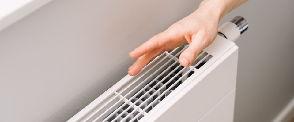 Person checking the condition of a home radiator to manage heating and reduce costs, promoting apartment energy efficiency.