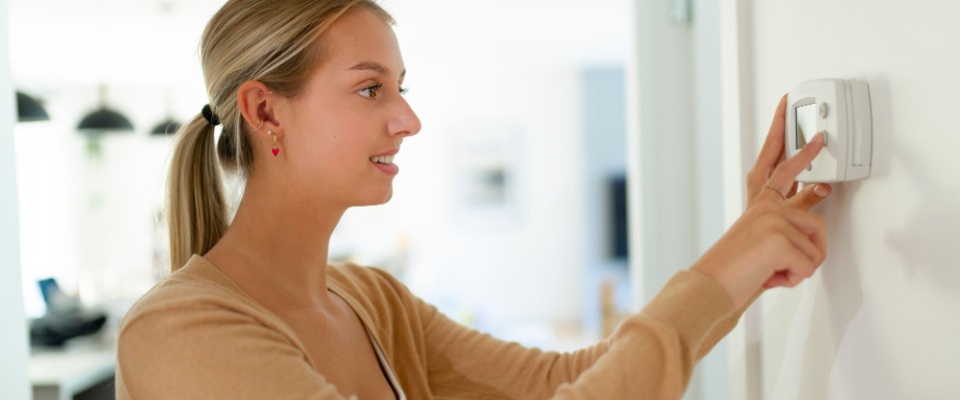 Woman adjusting a digital thermostat to control home temperature efficiently, an important and low-cost step for apartment energy efficiency.