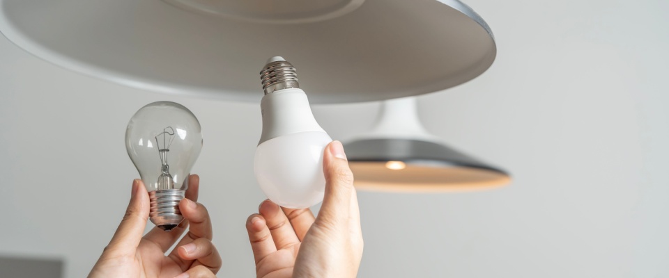 Person replacing an old incandescent bulb with an LED light, demonstrating simple upgrades that landlords or property managers can do to improve apartment energy efficiency.
