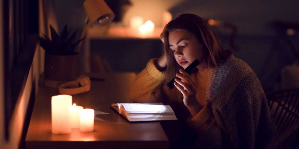 Woman using a flashlight and candles to read a book during a blackout, showing how to stay calm and prepared when the power goes out.