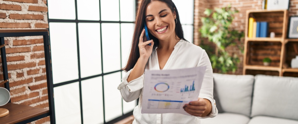 Smiling woman on the phone reviewing energy usage charts, discussing options for fixed-rate electricity plans to manage monthly bills.
