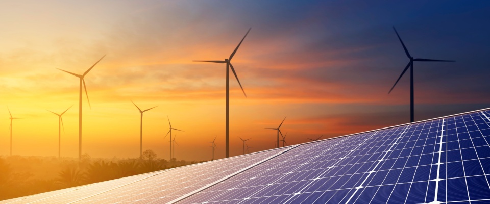 Solar panels and wind turbines at sunset, symbolizing renewable energy innovations that stem from the invention of electricity.