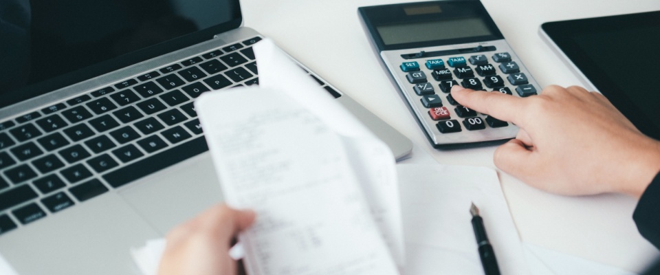 Person reviewing bills and using a calculator to compare costs, analyzing the best variable-rate electricity plan for home savings.