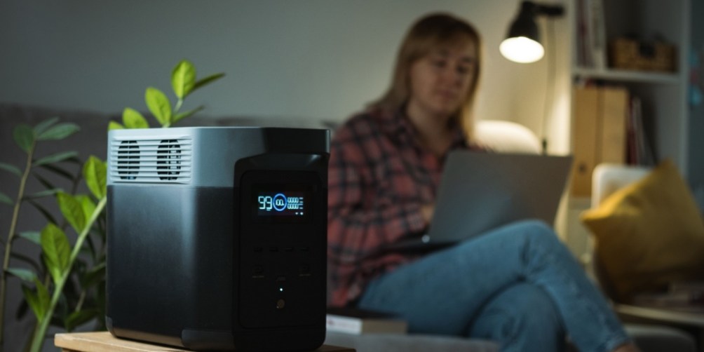 Portable power generator operating next to a couch while a person uses a laptop, illustrating everyday backup power for your apartment.