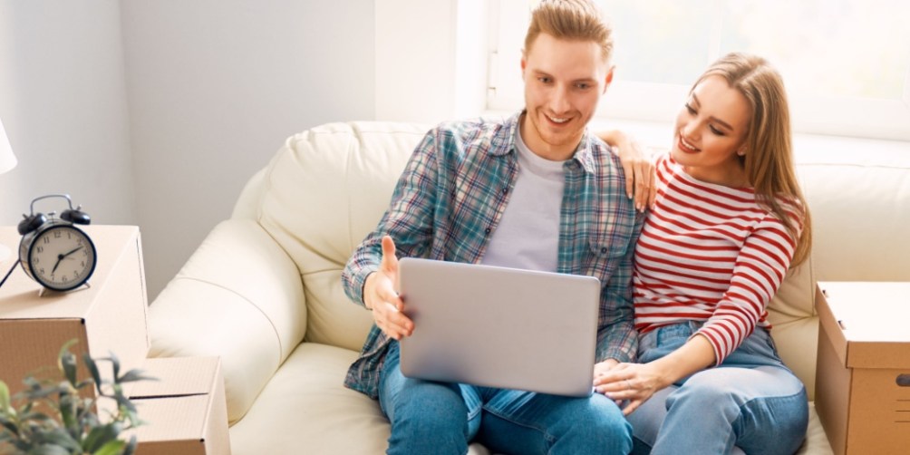Couple sitting on a couch with moving boxes while reviewing coverage on a laptop, taking time to compare renters insurance before moving.