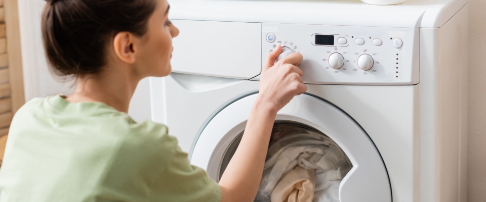 Person adjusting a washing machine cycle at home, showing how appliance use and efficiency affect Texas electricity rates for households.